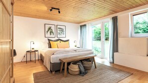 A bedroom with a bed, bedside tables, a window, and a view of greenery.