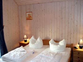 Quarto com parede revestida de madeira, cama com roupa de cama branca, duas mesas de cabeceira com luminárias e uma pequena imagem na parede.