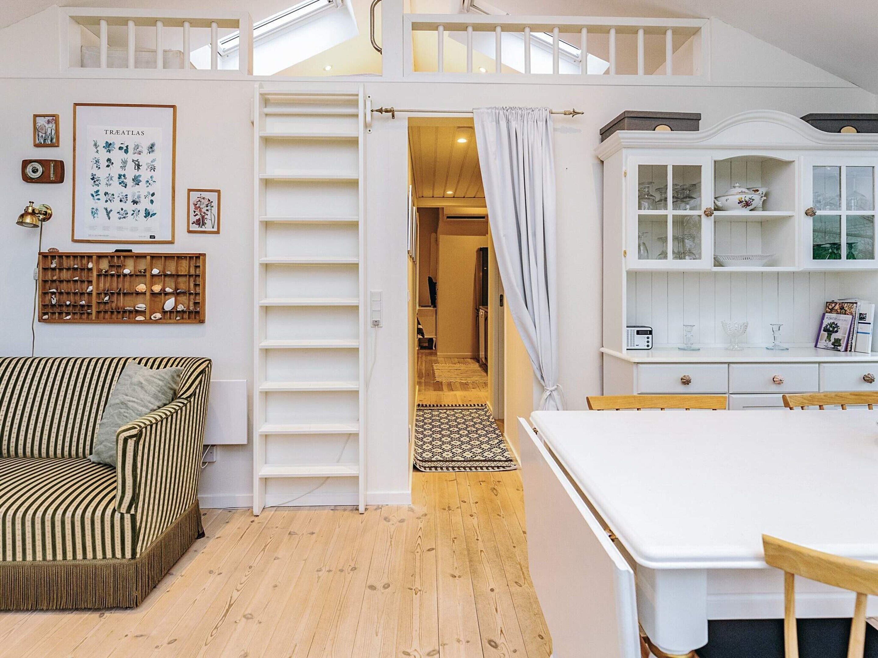 A cozy room with a striped sofa, a white cabinet with glass doors, and a wooden floor.