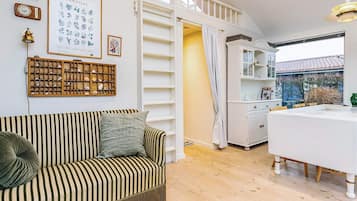 A cozy room with a striped sofa, a wooden display of shells, a framed botanical print, and a white dining table with chairs.