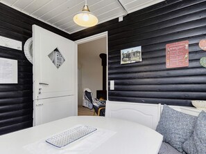 Une pièce avec un lit blanc, une porte blanche, un plafond blanc et des murs noirs. Un luminaire est fixé au plafond et un tableau encadré orne le mur.
