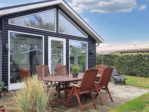 A modern house with a patio area featuring a wooden table and chairs, surrounded by potted plants. - 4 Person Holiday Home in Karrebaeksminde (Karrebæksminde)