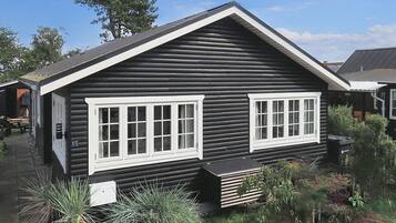 A log cabin with two white-framed windows, a small porch, and a sign indicating the number 15.