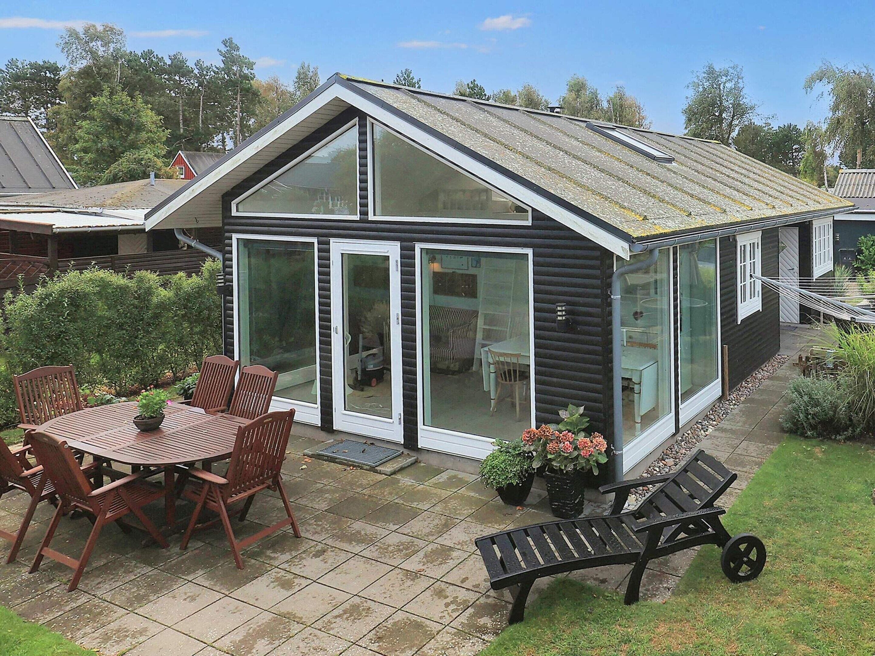 A modern house with a patio area, including a table and chairs, and a small garden with potted plants.
