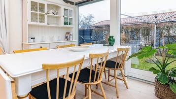 A modern kitchen with a white table, wooden chairs, and a large window overlooking a garden.