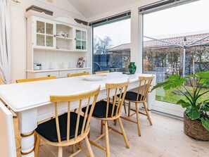 A modern kitchen with a white table, wooden chairs, and a large window overlooking a garden. - 4 Person Holiday Home in Karrebaeksminde (Karrebæksminde)