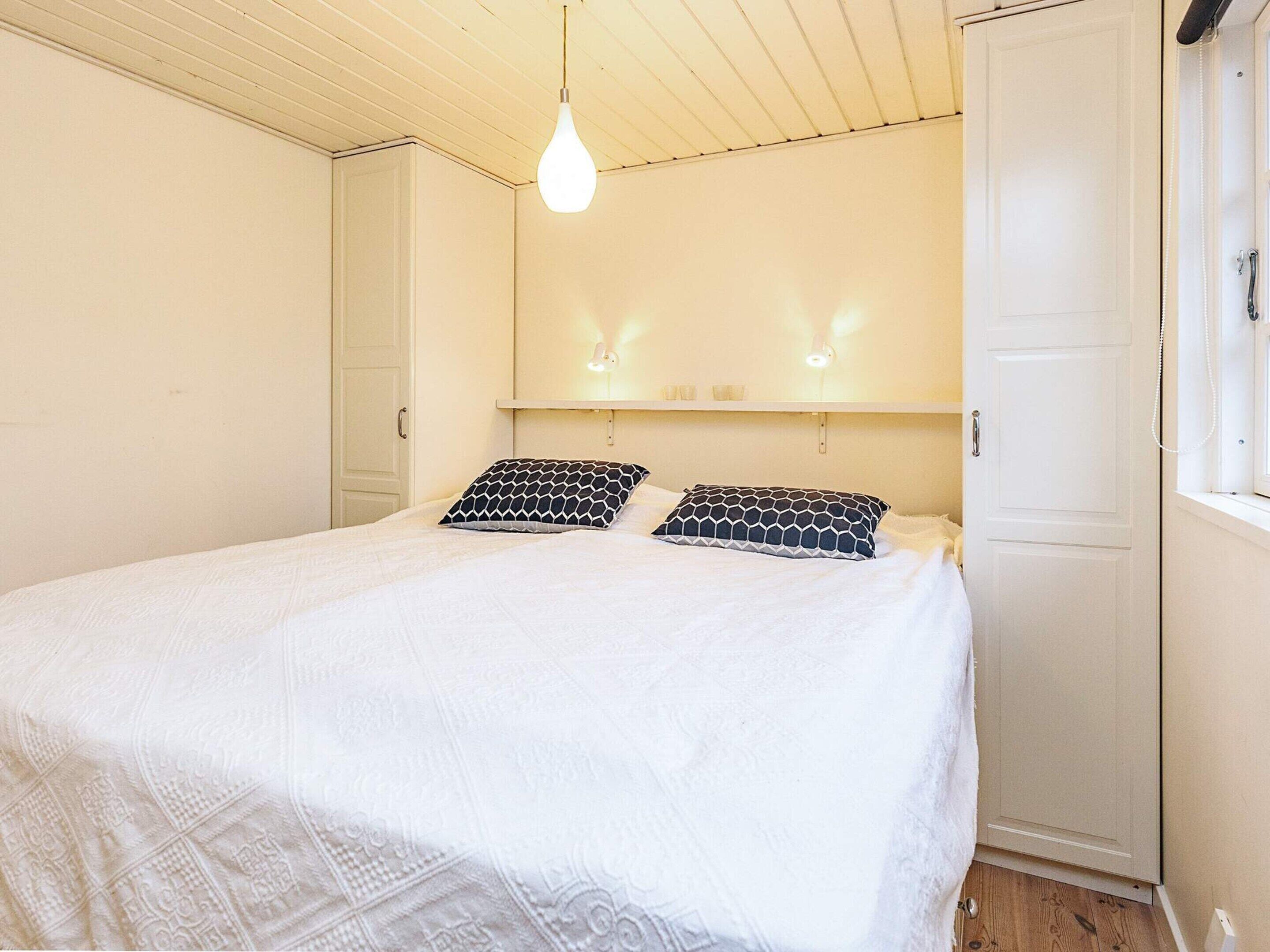 A bedroom with a bed, two pillows, a hanging light fixture, and a door.