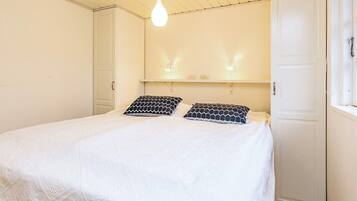 A bedroom with a bed, two pillows, a hanging light fixture, and a door.