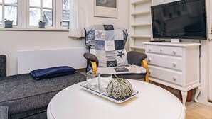 Un salón acogedor con un sofá, una mesa redonda con un centro de mesa decorativo, un televisor y un sillón de patchwork.