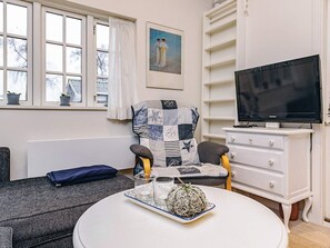 Un salon chaleureux avec un canapé, une table ronde agrémentée d’un élément décoratif, un téléviseur et un fauteuil à motifs.