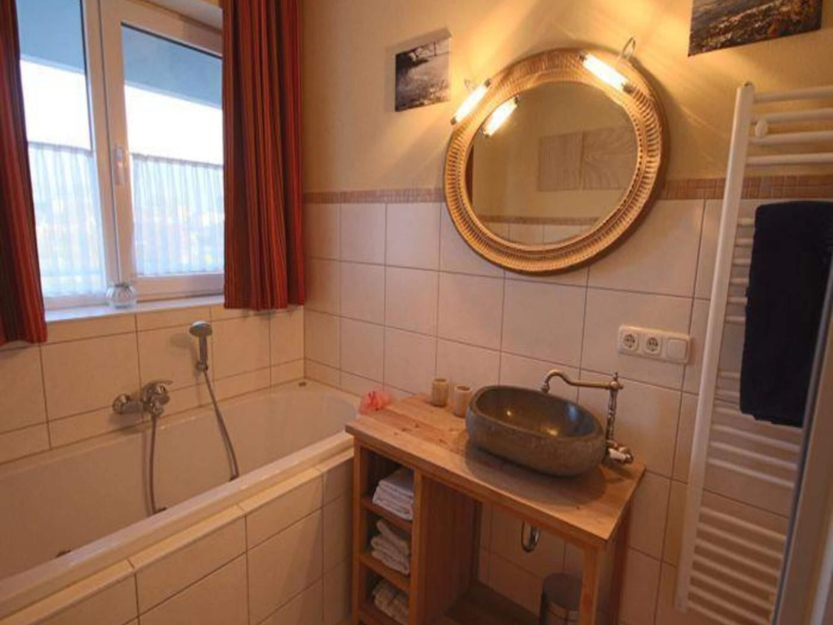 A bathroom with a bathtub, a sink with a basin, a mirror, and a towel rack.