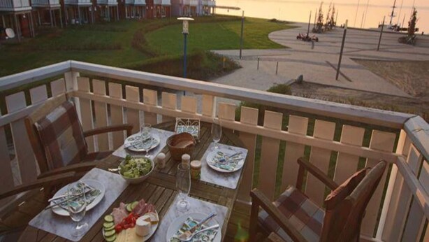 Ein Balkon mit Esstisch, mit Blick auf einen Strand und eine Reihung von Häusern.