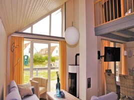 Habitación de hotel con un ventanal grande, un sofá, una mesa con un florero, un televisor de pantalla plana y una chimenea.