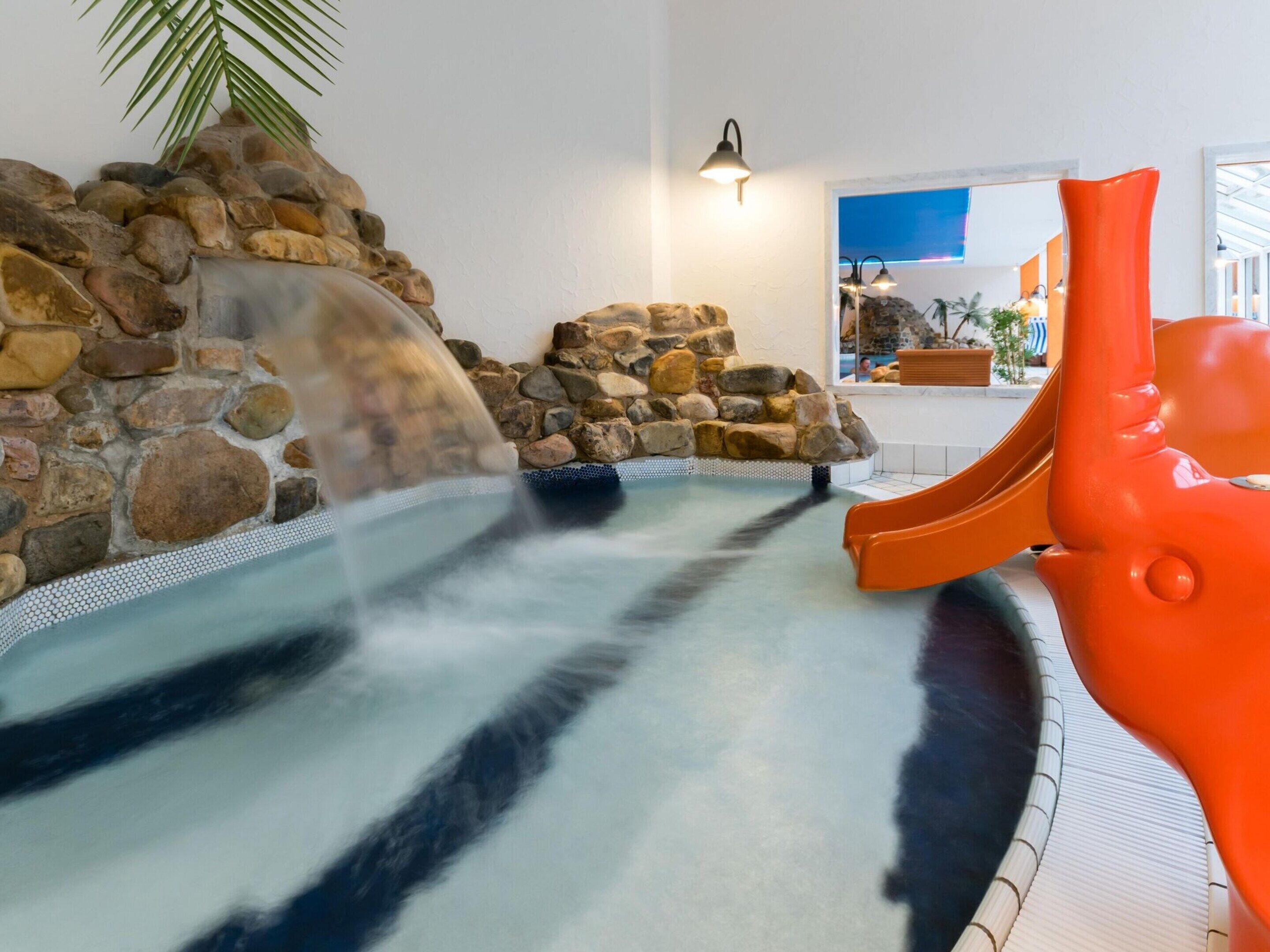 A hot tub with a waterfall feature, surrounded by a stone wall and a palm tree.