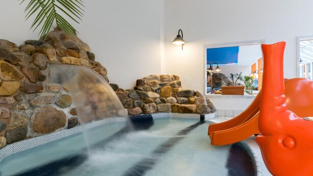 A hot tub with a waterfall feature, surrounded by a stone wall and a palm tree. - Appartement im Panoramic Hotel Bad Lauterberg (Bad Lauterberg)