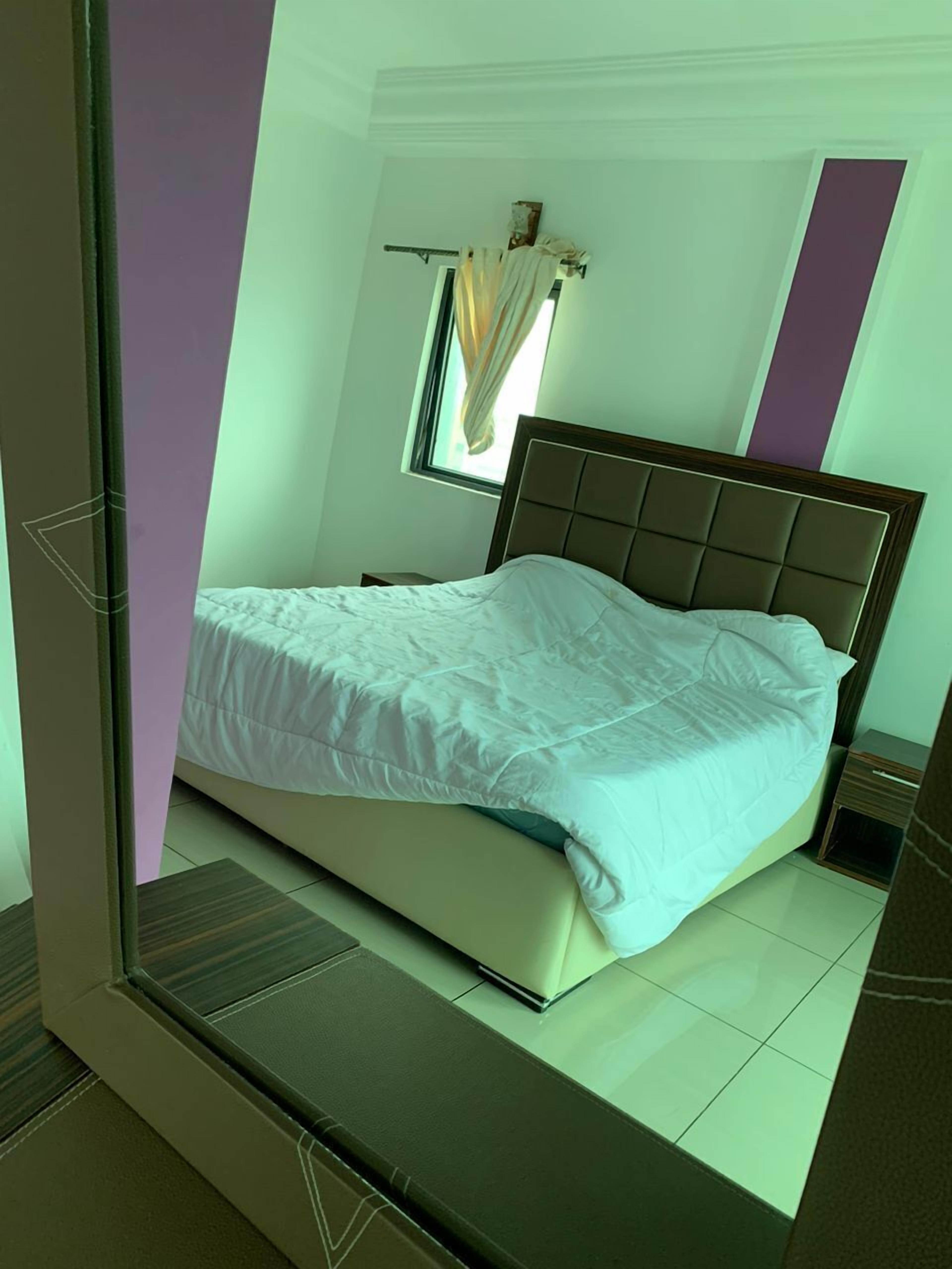 A neatly made bed in a room with a window and a small bedside table.