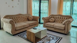 A living room with two beige sofas, a wooden coffee table, and a patterned rug. - Riyad City (Douala)