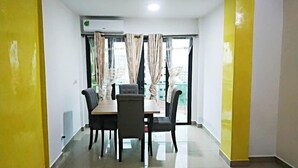 A room with a dining table and chairs, a window with curtains, and an air conditioning unit. - Riyad City (Douala)
