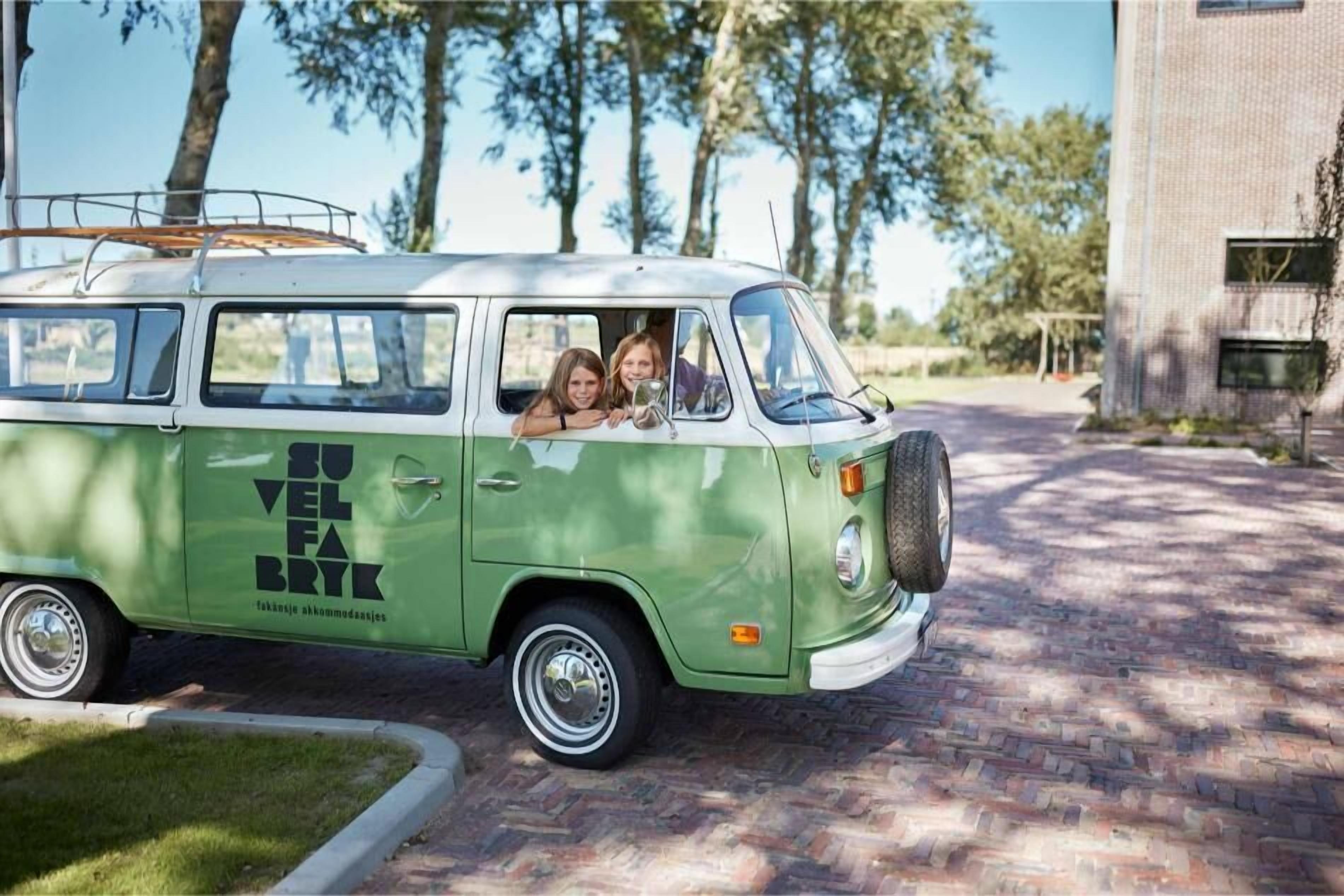 A green and white van parked on a brick driveway with a surfboard on the roof.