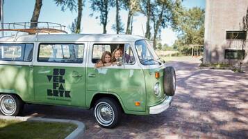 A green and white van parked on a brick driveway with a surfboard on the roof.