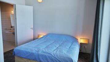 A bedroom with a bed, bedside lamps, a door to a bathroom, and a light fixture above the bed.