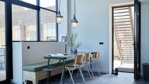 Un comedor moderno con un banco, mesa, sillas, lámparas colgantes y vistas al exterior.