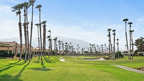 Een golfbaan met palmbomen, een heldere lucht en verre bergen.