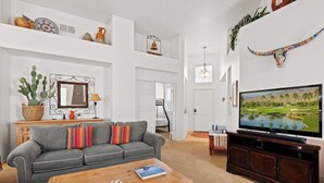 Een woonkamer met een grijze bank, een houten salontafel, een televisie op een houten standaard en een cactus aan de linkerkant.
