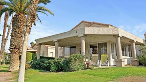 Een gebouw met een overdekte patio, palmbomen en een verzorgd gazon.