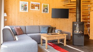 Un salon moderne avec un canapé d’angle gris, une table basse en bois, un tapis rouge, une cheminée et des murs en bois.