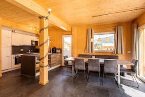 Enjoy communal dining with a central table and six chairs, surrounded by a clean, minimalist space with a kitchen area and large windows offering views of the surrounding landscape.