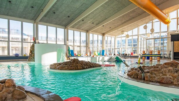 An indoor swimming pool with clear water, rock formations, and a children's play area. - Apartment in Holiday Park in Vederso Klit (Ulfborg)