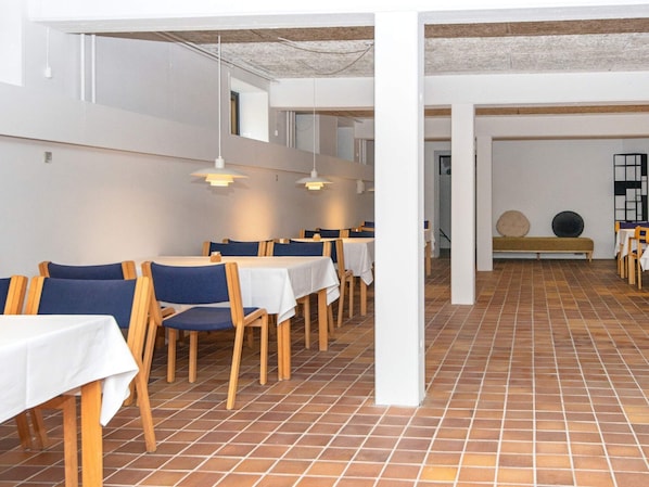 A restaurant with multiple tables and chairs, white walls, and tiled flooring. - Apartment in Holiday Park in Vederso Klit (Ulfborg)
