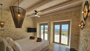 Une chambre dotée d’un grand lit, d’un ventilateur de plafond et offrant une vue sur le paysage depuis la porte.