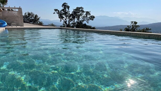 Une magnifique piscine à débordement, dont l’eau est d’une clarté parfaite, avec une vue sur les montagnes en arrière-plan.