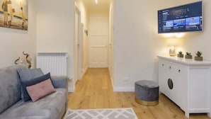 Ein modernes Wohnzimmer mit grauem Sofa, einem weißen Schrank, einem Flachbildfernseher und einem kleinen runden Hocker.