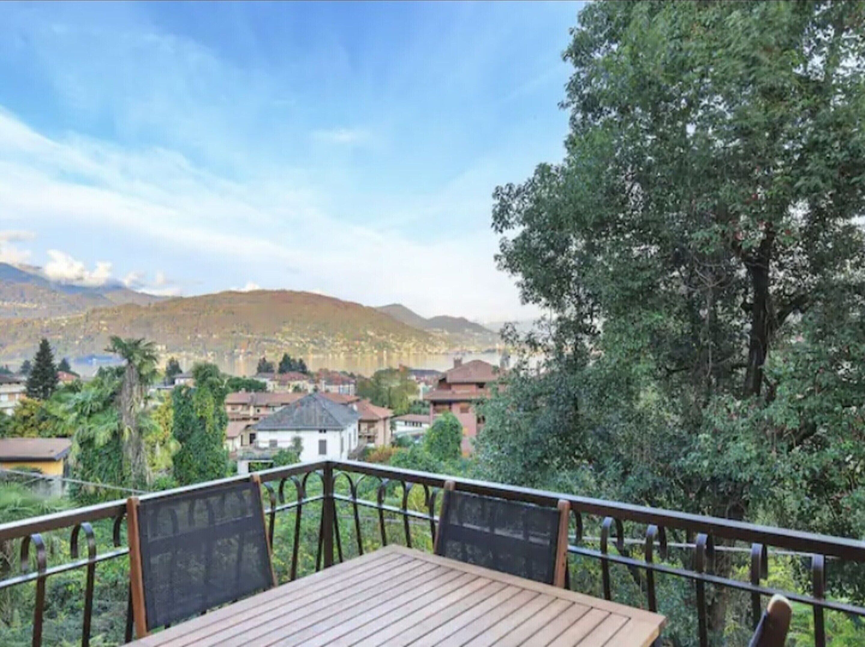 Eine Holzdielen-Terrasse mit Metallgeländern, die auf eine Stadt mit Häusern und Bergen im Hintergrund blickt.