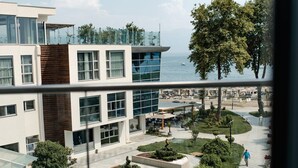 Un edificio moderno con facciata in vetro, un cortile con aree verdi curate e vista sul mare.