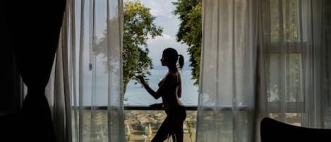 A room with a large window, a view of the sea, and two chairs.