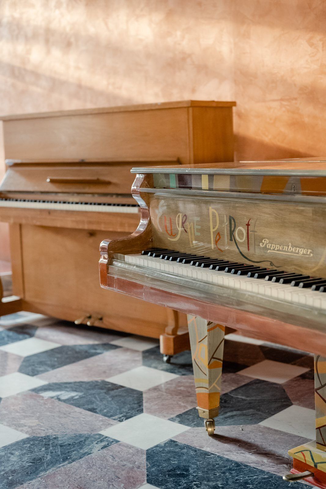 A grand piano with the inscription "Cure Pet" and "Cappenberger" on its side, placed in a room with a patterned tile floor.