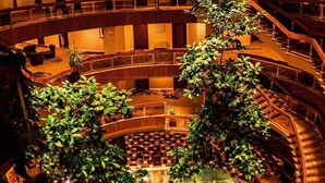 Un atrio a più livelli con una scala a spirale centrale, circondato da zone relax e piante in vaso.