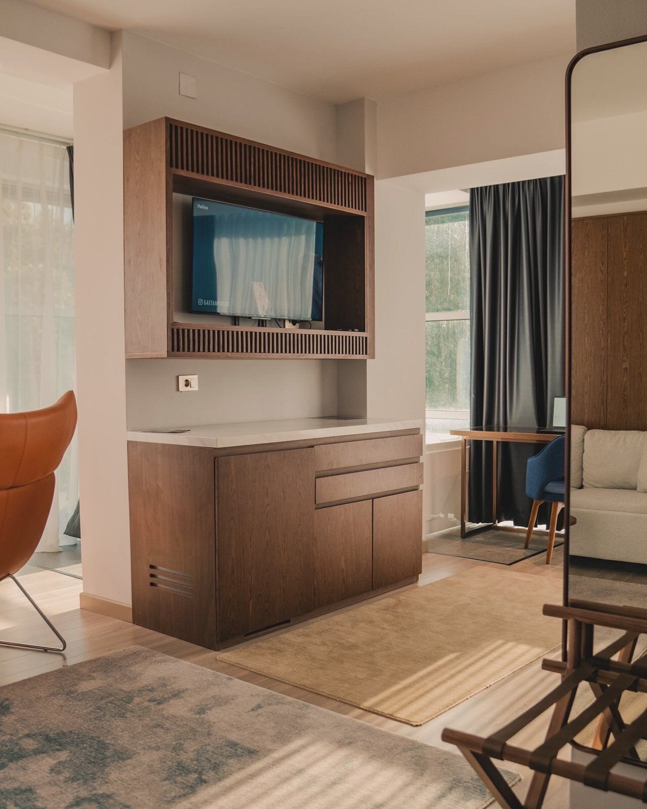 A modern living room with a wooden cabinet, a television, a sofa, and a chair.