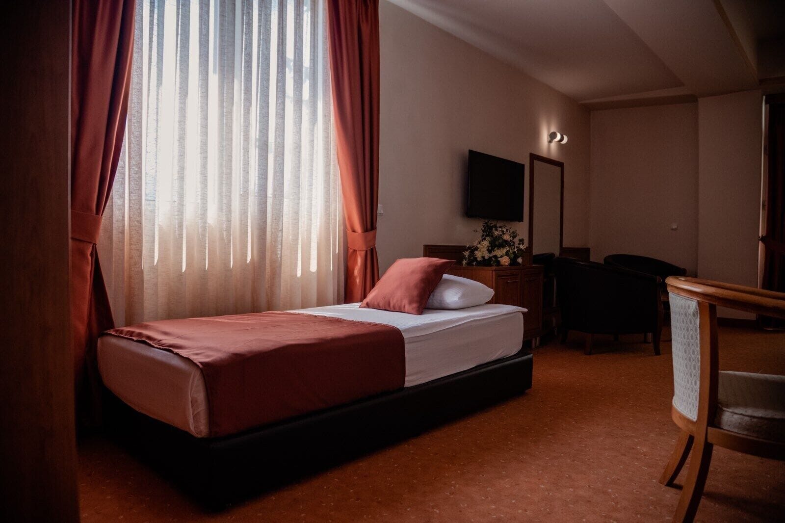 Une chambre d’hôtel avec un lit simple, un bureau, une chaise, une télévision et un miroir.
