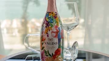 Una botella de vino Valdo Rose Brut sobre una mesa de vidrio con una copa de cristal transparente a su lado.