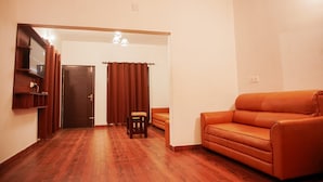 Un salon avec un plancher en bois, un canapé marron, une petite table et une porte avec des rideaux.