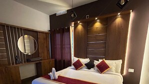 Une chambre d’hôtel moderne avec un grand lit, des panneaux de bois au mur, un grand miroir rond et un ventilateur de plafond.