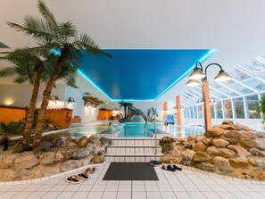 Ein tropisch gestalteter Innenpool mit Palmen und einer Felswand.