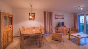 A cozy living room with a wooden dining table, a sofa, and a TV on a wooden cabinet. - Liebevoll Eingerichtetes Appartement (Rechlin)