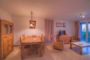 Una sala de estar acogedora con una mesa de comedor de madera, un sofá y un televisor sobre un mueble de madera.