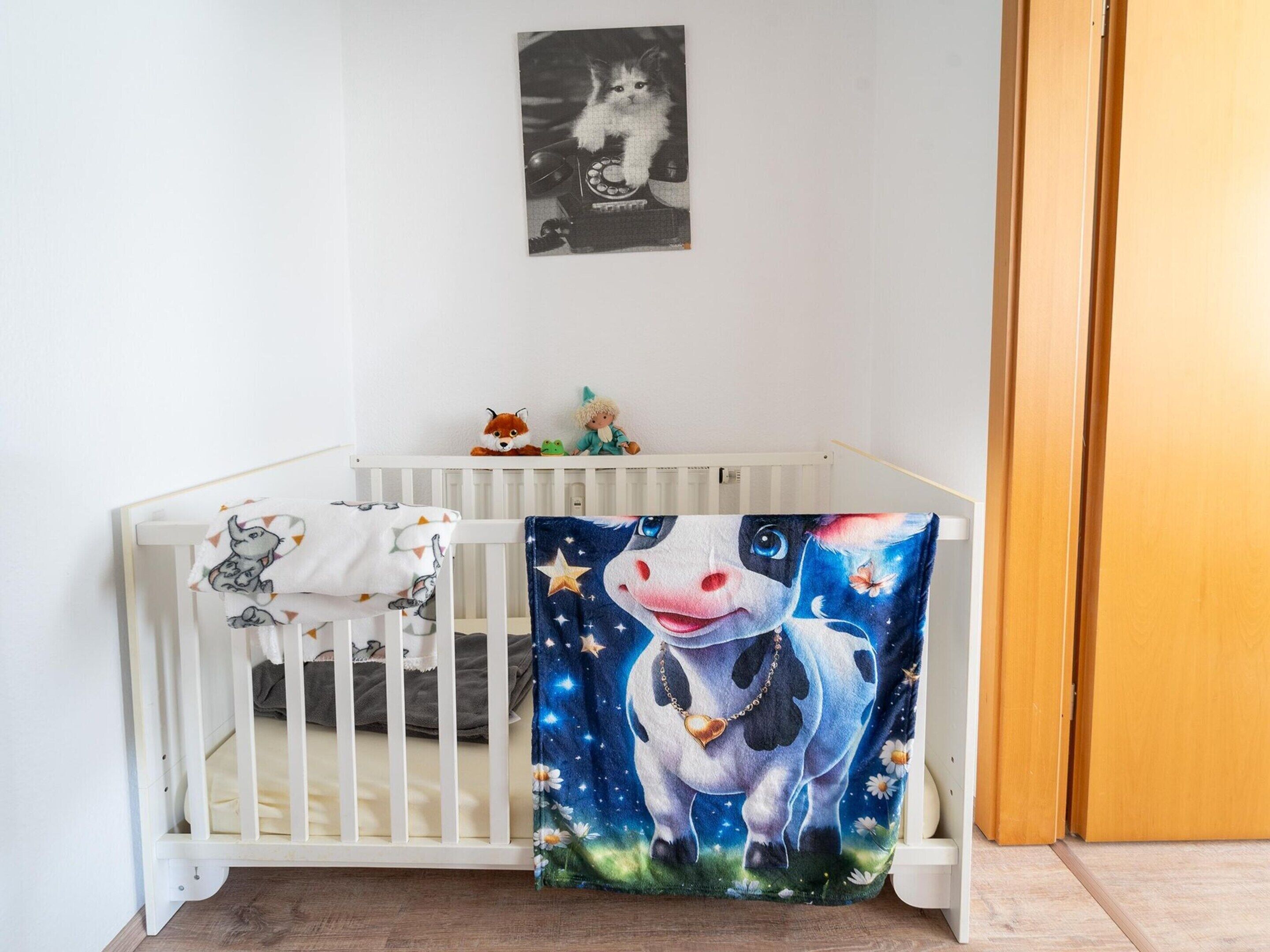 A white crib with a blanket and a wall-mounted picture.